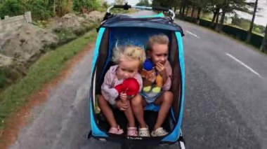 Küçük kız kardeşler yazın yolda bisiklet karavanına biniyorlar, kızlar 4 yaşında, babaları tarafından bisikletle götürülüyorlar. Yüksek kalite 4k görüntü