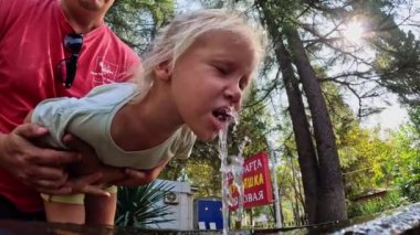 Küçük bir kız kuş çeşmesinden su içiyor, babaları onları kollarında tutuyor, yaz mevsiminde. Yüksek kalite 4k görüntü