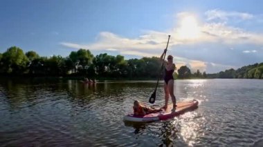Güneşli bir su yolunda dingin bir sahne beliriyor. Bir kadın pembe bir kürek tahtasında neşeli bir çocukla sakin suları keşfediyor.
