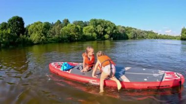 Bu video, denizdeki neşeli yaz anlarını vurguluyor, kırmızı kanolu kızları, kürek tahtasında bir kızı olan bir adamı, ve dengede duran çocukları gösteriyor, hepsi aile eğlencesini ve doğada kaynaşmayı kutluyor.