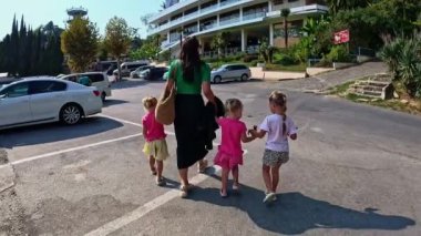 Üç kızı olan bir anne, yaz aylarında arka planda park alanında yürür. Yüksek kalite 4k görüntü