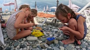 Küçük üçüz kız kardeşler Karadeniz 'in çakıl taşı sahilinde taşların üzerine resim yaparlar. Yüksek kalite 4k görüntü
