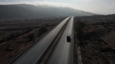 Türkiye 'de otoyol boyunca beyaz bir karavan sürüyor, İHA görüntüleri, kurumuş tarlalar ve kahverengi dağlar, güneş parlıyor. Yüksek kalite 4k görüntü