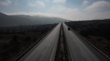 Türkiye 'de otoyol boyunca beyaz bir karavan sürüyor, İHA görüntüleri, kurumuş tarlalar ve kahverengi dağlar, güneş parlıyor. Yüksek kalite 4k görüntü