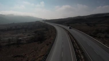 Türkiye 'de otoyol boyunca beyaz bir karavan sürüyor, İHA görüntüleri, kurumuş tarlalar ve kahverengi dağlar, güneş parlıyor. Yüksek kalite 4k görüntü