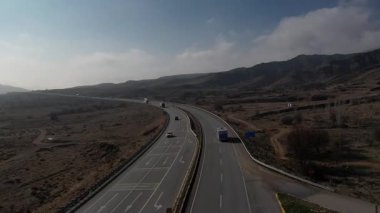 Türkiye 'de otoyol boyunca beyaz bir karavan sürüyor, İHA görüntüleri, kurumuş tarlalar ve kahverengi dağlar, güneş parlıyor. Yüksek kalite 4k görüntü