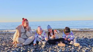 Annem ve üç küçük kızı kışın çakıllı bir deniz sahilinde oturuyorlar. Yüksek kalite 4k görüntü