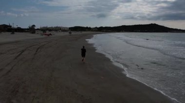 Kara giysili bir kız bulutlu havada denizin sahilinde koşar. Yüksek kalite 4k görüntü