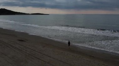 Kara giysili bir kız bulutlu havada denizin sahilinde koşar. Yüksek kalite 4k görüntü