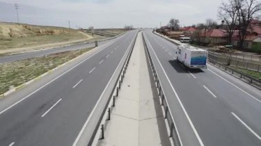 Baharda tarlalar arasında bir otoyol boyunca beyaz bir karavan dolaşır. Yüksek kalite 4k görüntü
