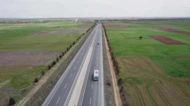Baharda tarlalar arasında bir otoyol boyunca beyaz bir karavan dolaşır. Yüksek kalite 4k görüntü