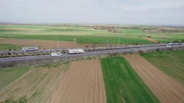 Baharda tarlalar arasında bir otoyol boyunca beyaz bir karavan dolaşır. Yüksek kalite 4k görüntü