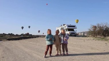 Kapadokya hindisinde beyaz bir karavanın ve balonların arkasında duran üç küçük kız kardeş. Yüksek kalite 4k görüntü