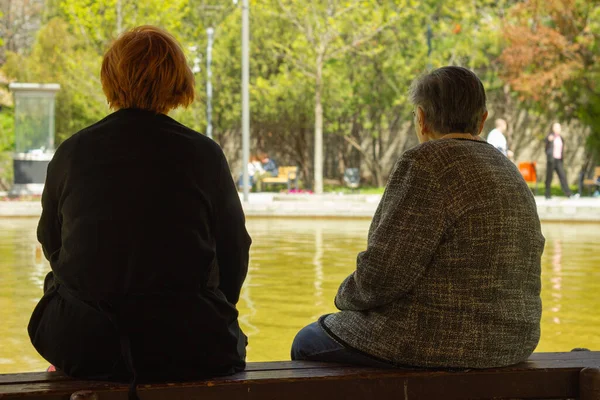 Two women enjoying the sun in the park. Two women, one old and the other middle-aged, sit in the park against the pool on a sunny day.