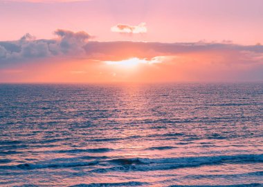 Pembe gökyüzü ve bulutlarla suyla gün batımı