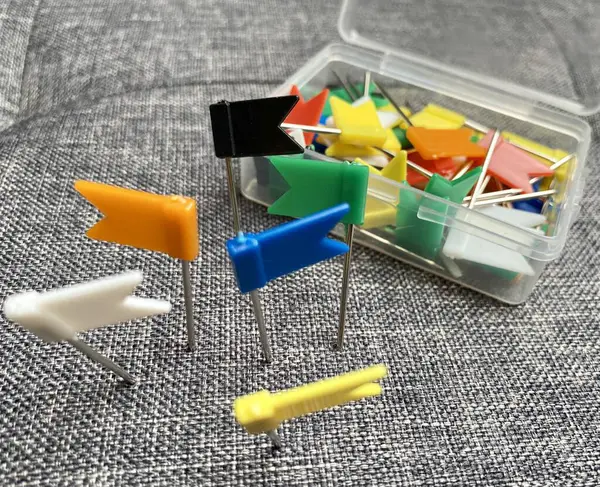 stock image Colorful push pins displayed beside a box filled with various flag markers on a gray sofa