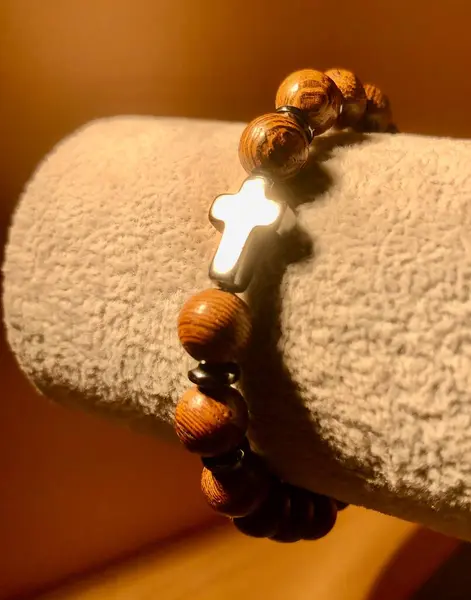 stock image A close-up view of a wooden rosary with a silver cross displayed on a soft velvet jewelry display in warm lighting