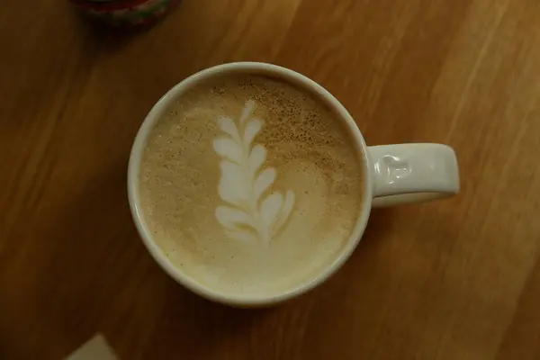 White coffee cup on wood with drawing of a flower in the coffee