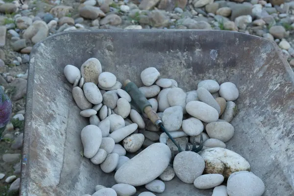 Taş, toprak ve taş ve kaldırım taşları gibi diğer doğal malzemelerle yüklü bir el arabası, bir küreğin yanında peyzaj ve inşaat projeleri için gereklidir.
