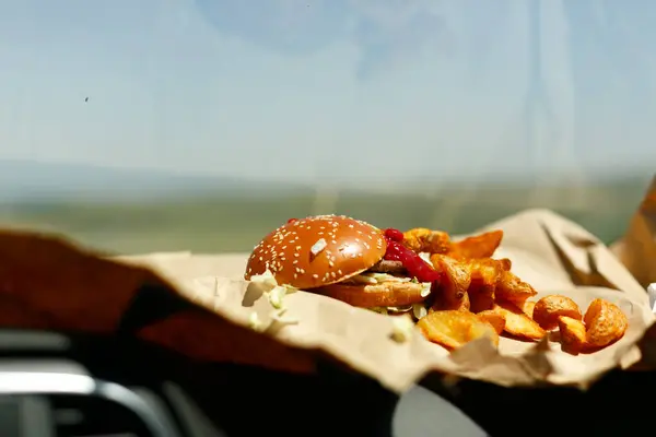 Bir araba konsolunda hamburger ve patates kızartması. Macera ve rahatlık hissi somutlaştırıyor.