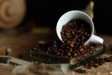 Estetik açıdan hoş bir kahve çekirdeği manzarası klasik bir beyaz bardaktan kırsal bir ahşap yüzeye dökülüyor.