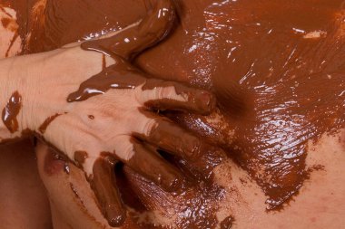 Zengin bir çikolatayı cilde ustalıkla uygulayan ve gerçekten eşsiz bir sanat konseptini sergileyen ellerin yakın plan görüntüsü.