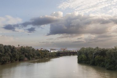 Yeşillik ve dramatik bulutlarla dolu sakin bir nehir manzarası, doğal temalı projeler ve ilham kaynakları için ideal.