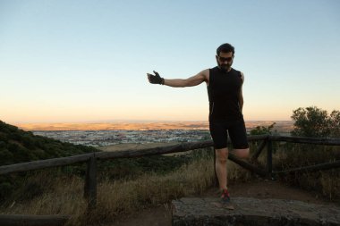 Bir adam, doğa yürüyüşünün tadını çıkarırken nefes kesici bir günbatımı arka planına karşı kendine güvenen bir poz verir.