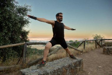 Erkek bir atlet, gün batımının nefes kesen görüntüsüyle mükemmel bir şekilde tamamlanmış bir yoga pozu sergiliyor.