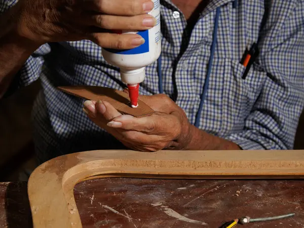 Bir marangoz atölyesinde, çok yetenekli bir zanaatkar özenle ahşap bir parçaya yapıştırıcı sürer.