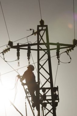 Tecrübeli bir elektrikçi nefes kesici bir günbatımı arka planının altında yüksek voltajlı elektrik hatlarını koruyor.