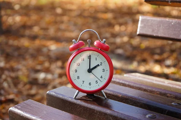 The concept change time. Alarm clock on a wooden bench in the autumn park.