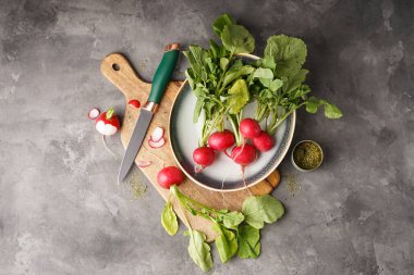 Tabağında yapraklar olan taze kırmızı turp ve gri arka planda tahta kesme, düz yatış. Üst görünüm.