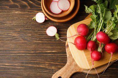 Fresh red radish and kitchen board on wooden background, top view. Space for text.