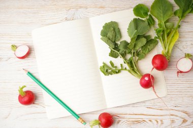 Taze kırmızı turp ve beyaz ahşap arka planda defter, metin için boşluk. Düz yatıyordu.