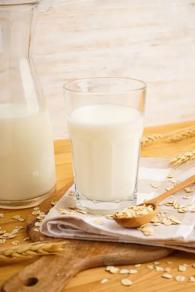 A glass of oat milk, a jug and oat flakes on a wooden background, vertically.
