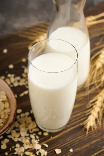 Oat milk in the glass with jug of milk and oat on a wooden background. The concept of a vegetarian diet.