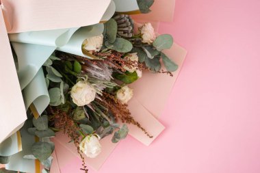 Beyaz güller, protea, yeşil esmer ve pembe arka planda okaliptüs dalları olan güzel bir buket. Düz yatıyordu.