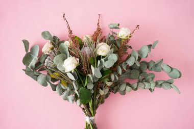 Pembe arka planda beyaz güller, protea, esmer ve okaliptüs dallı güzel bir buket..