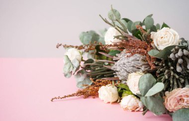 Beyaz güller, protea, yeşil esmer ve okaliptüs dallı güzel buket pembe arka planda, metin için boşluk.