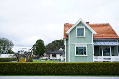 Norveç 'teki geleneksel bir İskandinav evinin yan perspektifi, açık yeşil ahşap paneller, parlak turuncu kiremitli çatı ve klasik beyaz veranda.
