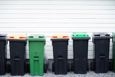 Ayrı atık toplama için farklı renklerde kapaklı bir sıra çöp kutusu: plastik, kağıt, cam, organik atık ve genel çöp. Geri dönüşüm, sürdürülebilirlik ve çevre dostu atık yönetimi kavramı.