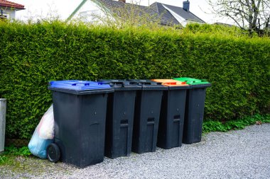 Ayrı atık toplama için farklı renklerde kapaklı bir sıra çöp kutusu: plastik, kağıt, cam, organik atık ve genel çöp. Geri dönüşüm, sürdürülebilirlik ve çevre dostu atık yönetimi kavramı.