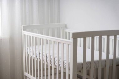 Temiz, modern, minimalist, ahşap döşemeleri ve katıksız perdeleri olan bir bebek odasına yerleştirilmiş bir bebek beşiği. Bebekler için rahat ve güvenli bir uyku ortamı.