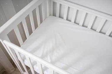 Minimalist, parlak bir bebek odasına yerleştirilmiş, temiz, modern, minimalist bir bebek beşiği. Bebekler için rahat ve güvenli bir uyku ortamı.