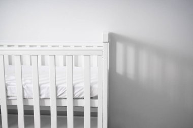 Temiz, modern, minimalist, ahşap döşemeleri ve katıksız perdeleri olan bir bebek odasına yerleştirilmiş bir bebek beşiği. Bebekler için rahat ve güvenli bir uyku ortamı.