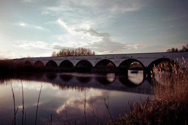 Gün batımında nehrin üzerinde eski bir taş köprü