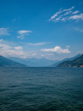 Bulutlu bir gökyüzünün altında dağlarla çevrili güzel bir gölün görüntüsü.