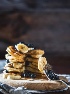 Kırsal bir tahta üzerinde yabanmersini, muz ve bal şurubuyla pişirilmiş Amerikan krepleri. Kahvaltıda lezzetli ve sağlıklı bir tatlı..