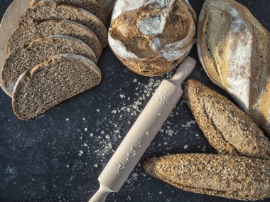 Taze çörek, tam buğday ekmeği, ekşi ekmek ve merdane ve un ile kesilmiş ekmek. Kırsal granitin siyah arka planında. Kopyalamak için boşluk.